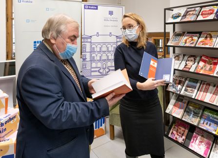 A photograph. The director of the villa Decius institute for culture, Dominika Kasprowicz, gives the books to the director of the Krakow library, Stanisław Dziedzic. In the backgound a tall shelf full of books.